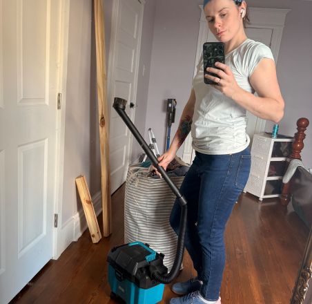 A person wearing rubber gloves cleaning a dirty gas stove with a cloth and spray bottle.
